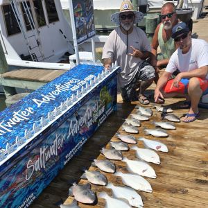 Three anglers with flounder limit displayed on dock behind Saltwater Adventures branded fish box at Ocean City Maryland marina after bay fishing charter