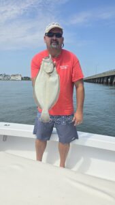 Angler holding large flounder on boat with Route 50 bridge in background during Ocean City Maryland fishing charter
