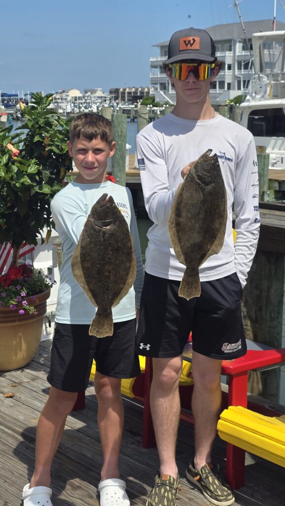 Two teenage anglers holding flounder at Ocean City Maryland marina after bay fishing charter