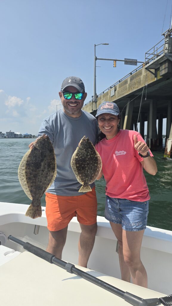 Couple holding flounder with Route 50 bridge in background during Ocean City Maryland fishing charter