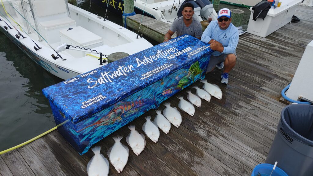 Two anglers with flounder limit displayed behind Saltwater Adventures branded fish box at Ocean City Maryland marina